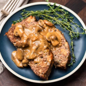 Blue plate with 2 slices of meatloaf topped with brown mushroom gravy.